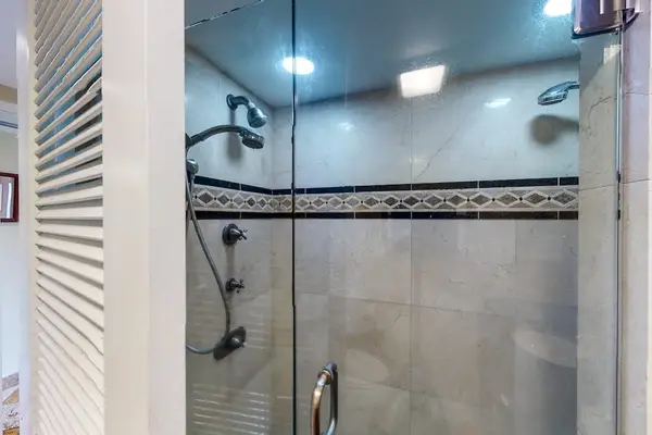 Walk-in shower features glass doors, tiled walls, and grab bars