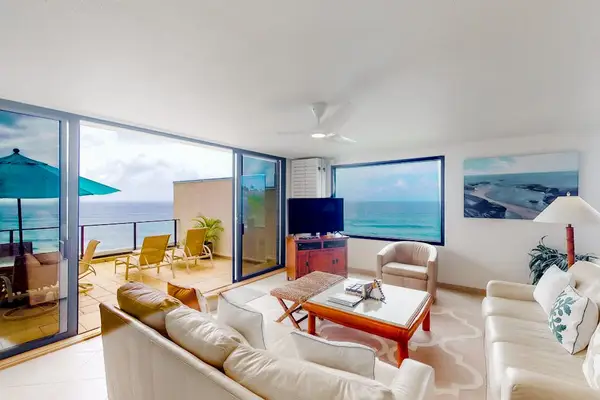 Ocean-view living room features comfortable seating, bright windows, and artwork