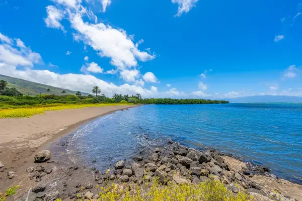 Rocky shoreline frames calm Pacific waters beneath bright island skies