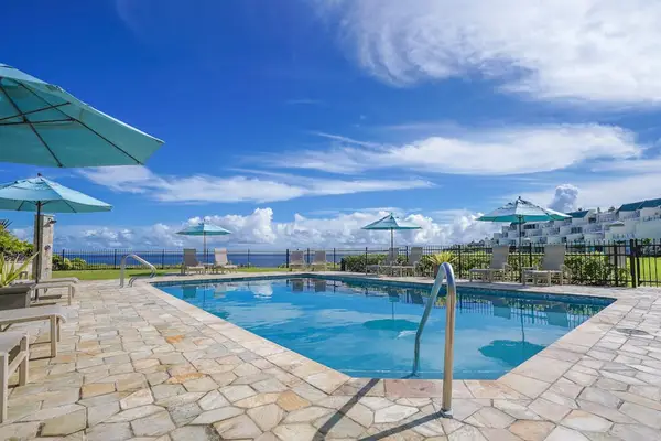 Coastal pool setting overlooks ocean horizons, green lawns, and skies