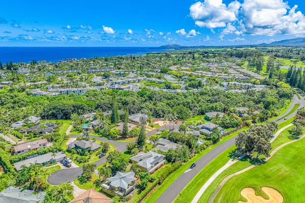 Aerial view of a neighborhood in Princeville, Kauai, featuring homes surrounded by lush greenery and close proximity to the ocean
