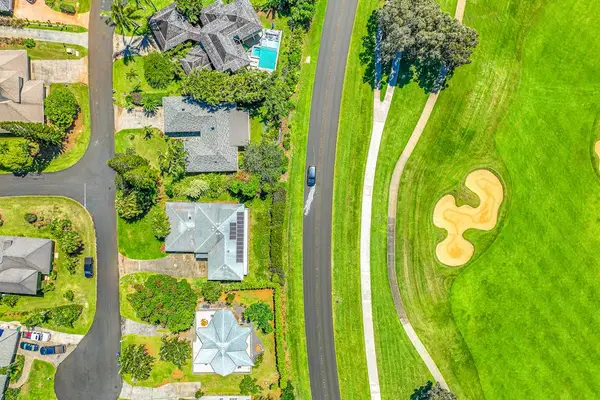 This aerial view shows homes along a road adjacent to a green golf course fairway in Princeville
