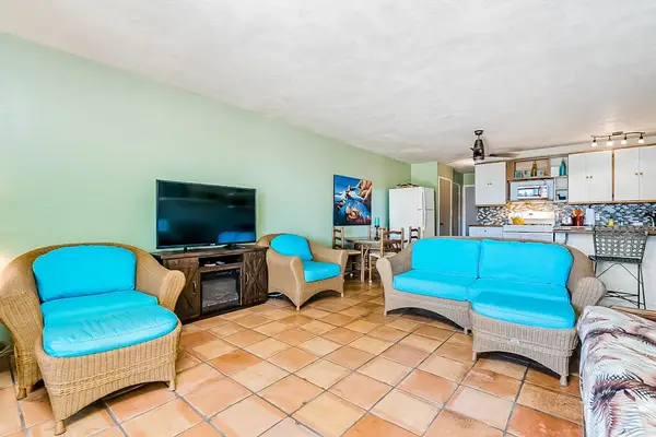Open living area combines turquoise seating, television, kitchen, and sunlight