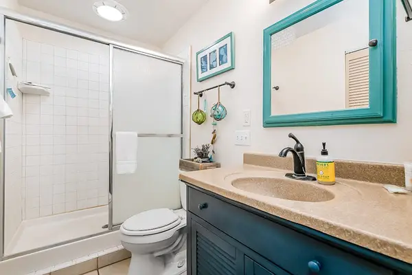 Full bathroom features glass shower, toilet, vanity, and turquoise accents