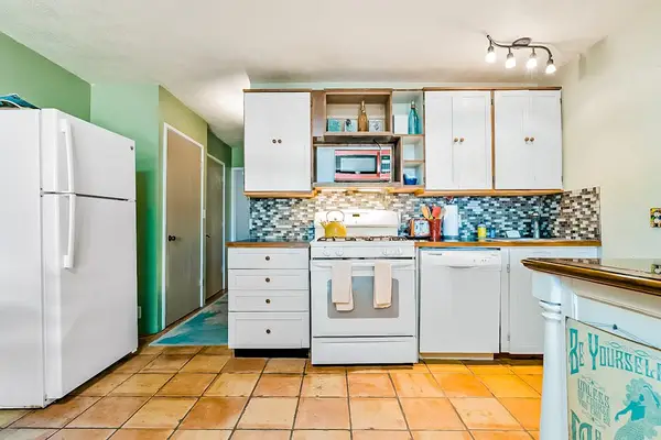 Bright kitchen showcases white cabinetry, refrigerator, patterned backsplash, and island