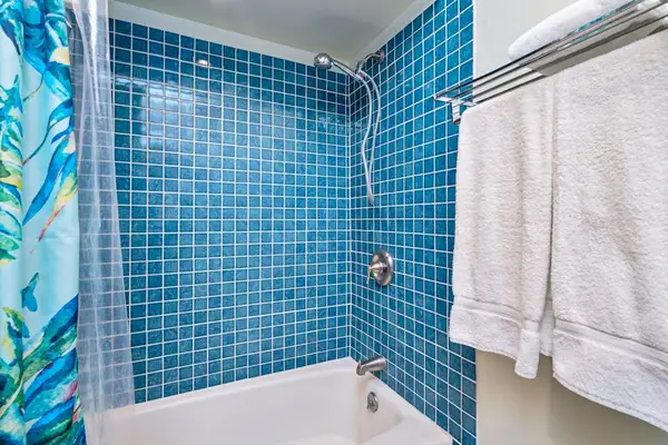 Tiled shower area includes glass doors fixtures and hanging towels