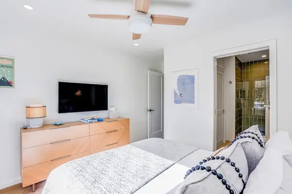 Modern Bedroom Layout with Wall-Mounted TV, Light Wood Dresser & Glass Shower View