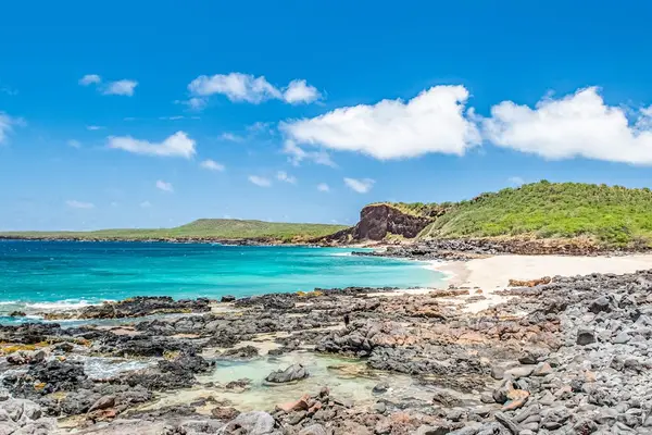 Nearby coastline reveals turquoise water, rocky shore, hills, and clouds