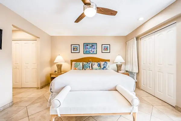Bright bedroom features comfortable bed ceiling fan and storage