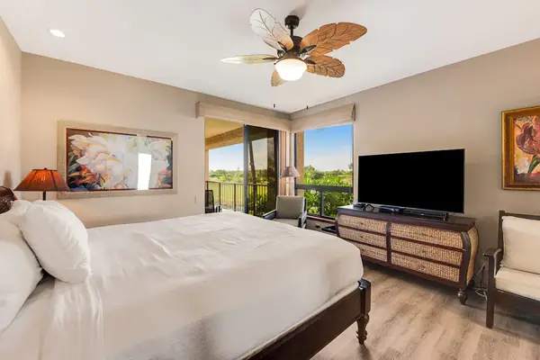 Bedroom view includes bedding, television, windows, palms, and fairway scenery