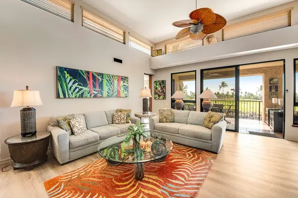 Open lounge displays sofas, television, ceiling fan, windows, and artwork