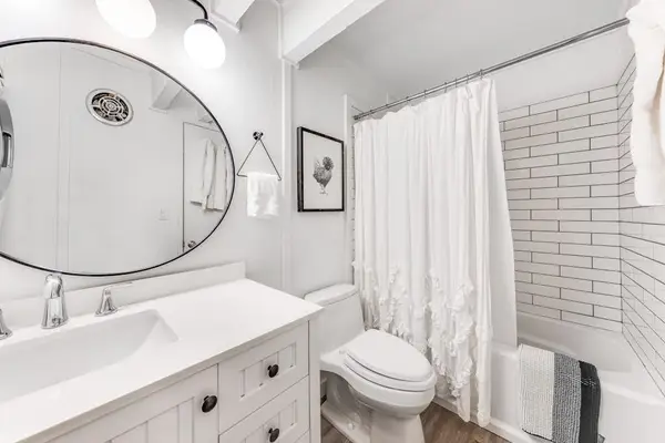Round mirror brightens tidy bathroom with tub shower and vanity