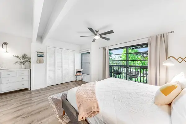 This bedroom features soft linens airy windows and island greenery