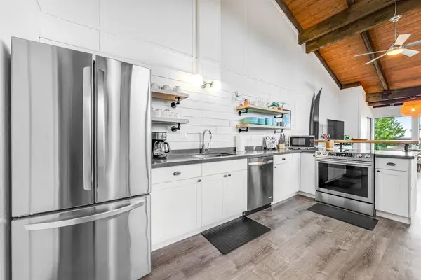 Stainless refrigerator anchors clean kitchen beneath warm exposed beams overhead