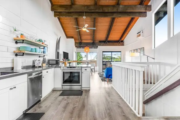 Long bright kitchen flows toward stairs beneath dramatic timber beams