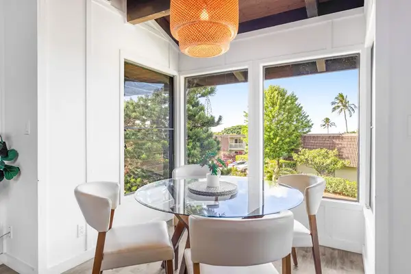 Sunlit breakfast nook overlooks greenery through wide windows and doors