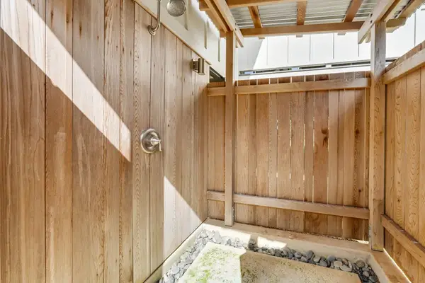 Outdoor shower area features wood fencing, pebbles, and natural light