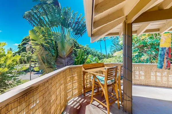 Balcony seating overlooks tropical greenery beside bright open-air living areas