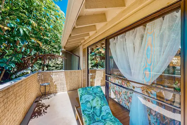 Covered balcony offers cushioned seating, curtains, greenery, and island air