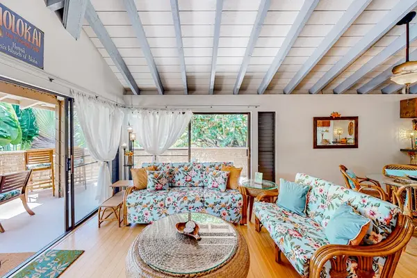 Living room features patterned seating, coffee table, artwork, and windows
