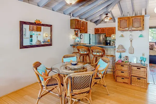 Dining area features rattan chairs, artwork, kitchen cabinetry, and table