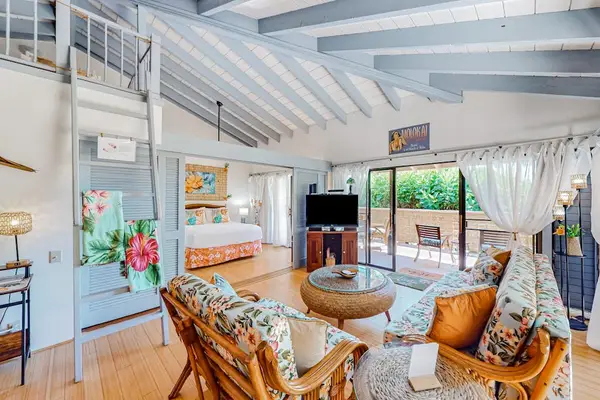 Living room offers rattan seating, television, plants, and garden access