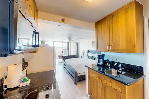 Dark granite countertops, wood cabinetry, small sink, microwave, and view looking into the primary living space.