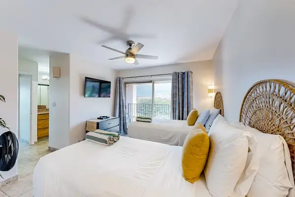 This modern oceanfront condo bedroom features a ceiling fan and a balcony overlooking the water.