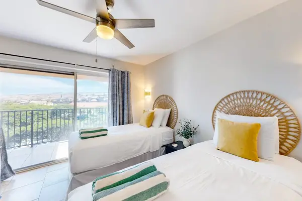 This modern oceanfront condo bedroom features a ceiling fan and a balcony overlooking the water.