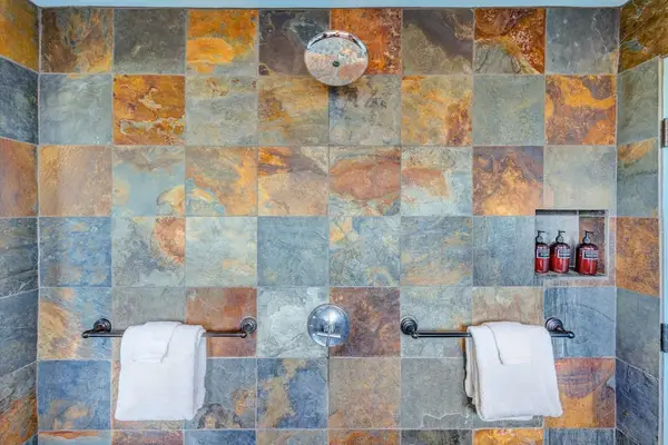 Stone-tiled spacious shower featuring necessities