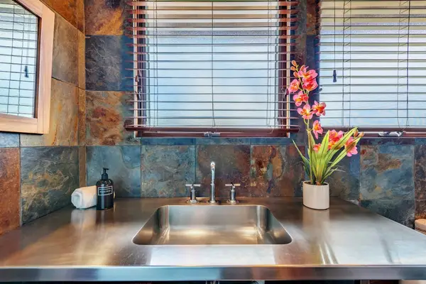 Vanity showcases a stainless sink, stone walls, and floral accents