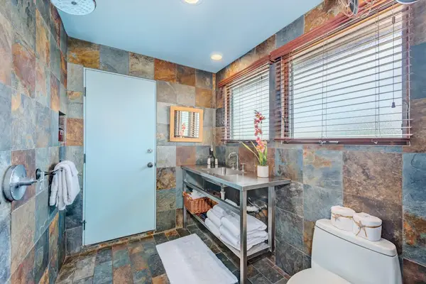 Stone-tiled bathroom features open shelving and clean toilet.