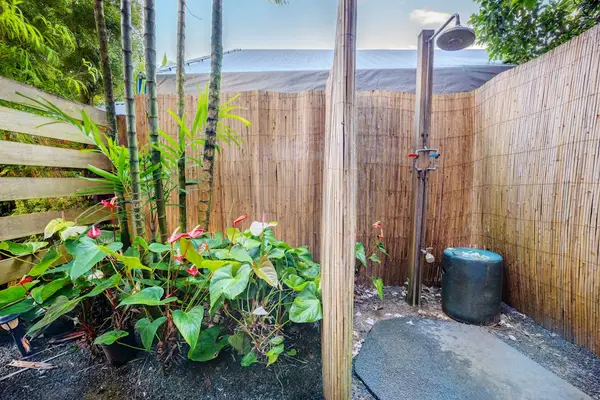 Outdoor shower area features fencing, tropical plants, and natural light