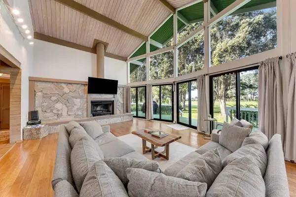 Deep sectional seating faces stone fireplace beneath dramatic garden windows