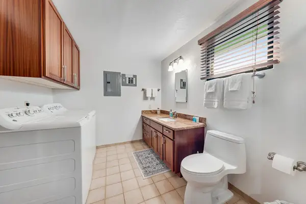 Washer and dryer sit beside bright vanity and tiled bath