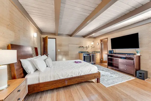 King bed faces television across airy suite with timber beams