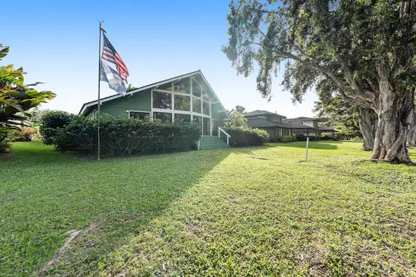 Sunny lawn frames welcoming home beneath towering trees and flag