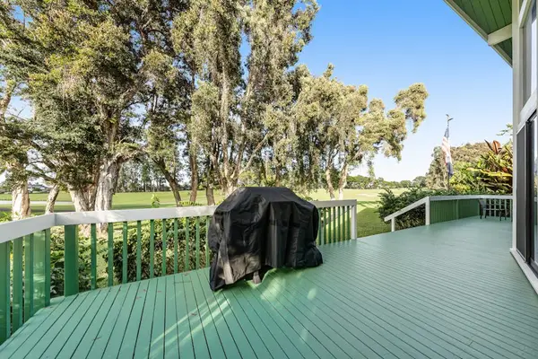 Covered grill stands ready on green deck beside leafy grounds