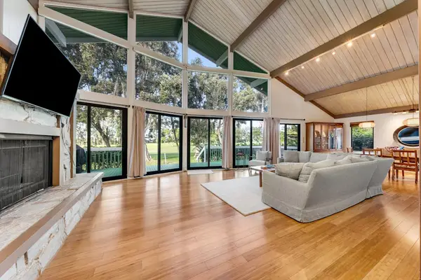 Vaulted living room frames forest views beside fireplace and sofas