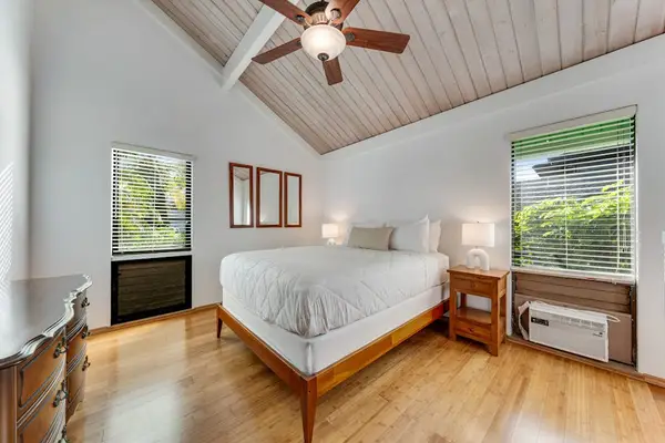 Queen bed rests below vaulted ceiling beside bright leafy windows