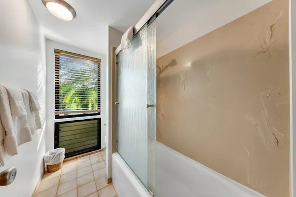 Glass shower reflects leafy light beside neutral tile and towels