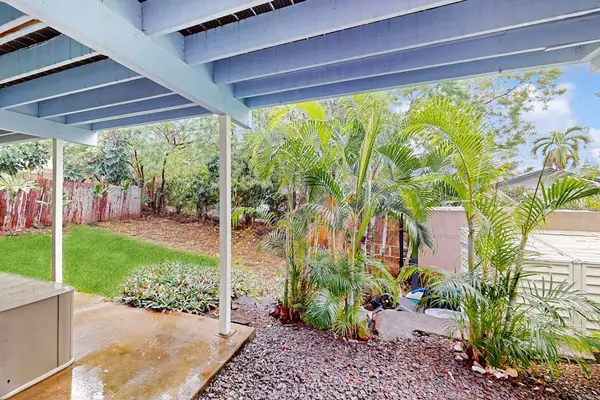 Lush tropical backyard view looking out from the shade of the covered patio and custom blue pergola! 🌴✨