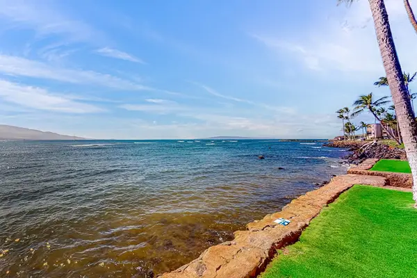 Oceanfront manicured lawns, swaying palm trees, and turquoise Pacific waters create a picture-perfect setting as waves gently crash along the shoreline.