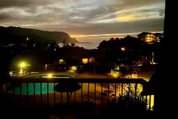 Twilight pool gleams beneath mountain silhouettes amid softly illuminated gardens
