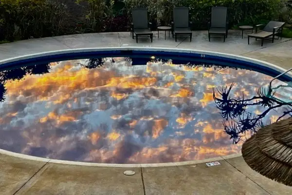 Sunset clouds reflect across circular hot tub beside quiet lounge chairs
