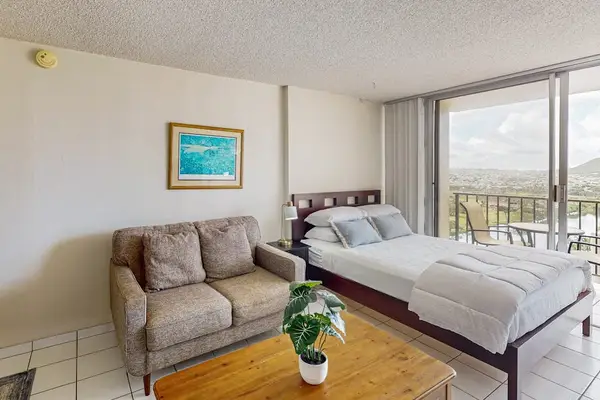 Bright studio with queen bed, sofa, and balcony views