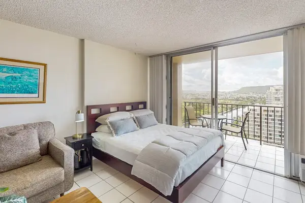 Queen bed and sofa beside bright balcony doors