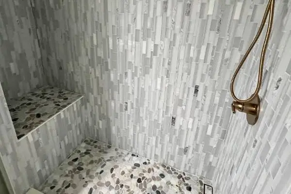 Walk-in shower features tiled walls, handheld fixture, and corner bench