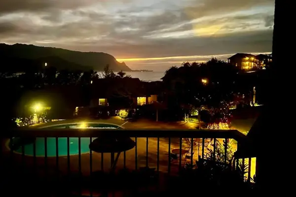 Evening balcony overlooks illuminated pools, gardens, and peaceful resort grounds