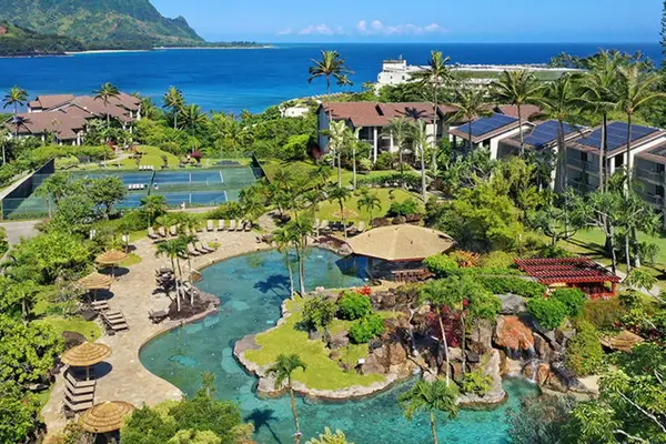Aerial resort view reveals pools, gardens, courts, and ocean scenery